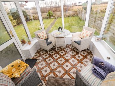 A sunroom with four chairs a round glass table and windows overlooking a garden at Arcadie in Amble