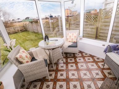 A conservatory with wicker chairs cushions a glass table binoculars and a garden view at Arcadie in Amble
