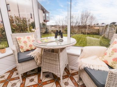 A sunroom with a glass table and two wicker chairs with cushions and blankets at Arcadie in Amble