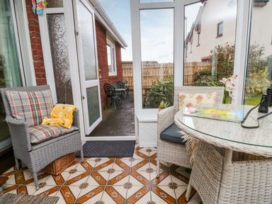 A conservatory with wicker chairs a glass table and a view of the garden at Arcadie in Amble
