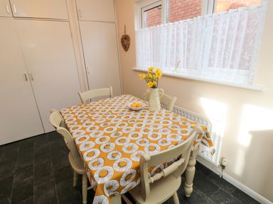 A dining area with a table covered by a patterned tablecloth and chairs near windows with lace curtains at Arcadie in Amble