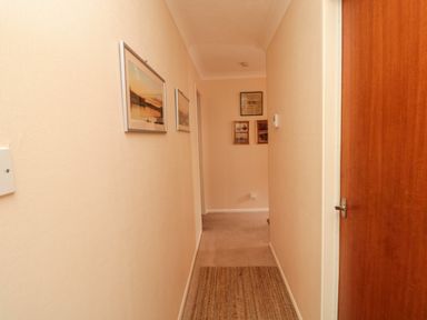 A hallway with framed pictures on the wall a wooden door and a woven rug on the floor at Arcadie in Amble