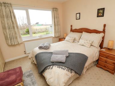 A bedroom with a double bed wooden headboard two bedside tables lamps and a window with curtains at Arcadie in Amble
