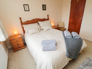 A bedroom with a double bed pillows bedside tables lamps and folded towels at Arcadie in Amble