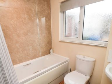 A bathroom with a bathtub, toilet, frosted window, and a shower curtain at Arcadie in Amble