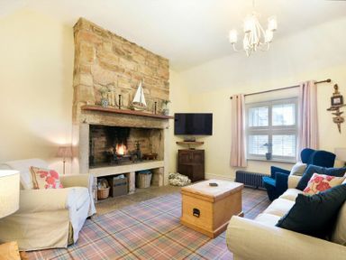 A living room with a stone fireplace a TV on the wall sofas and armchairs around a wooden chest at Charlton Cottage in Bamburgh