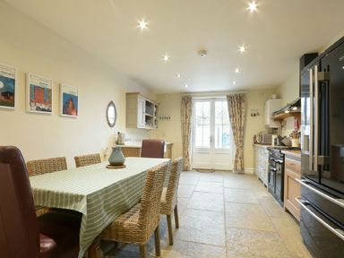 A kitchen with a dining table and chairs a refrigerator oven cabinets and double doors with curtains at Charlton Cottage in Bamburgh