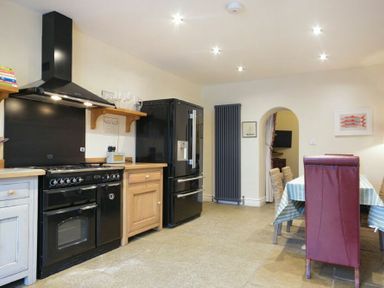 A kitchen with a black oven, black refrigerator, wooden cabinets, dining table with chairs and arched doorway at Charlton Cottage in Bamburgh