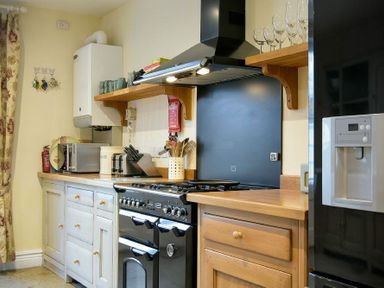 A kitchen with wooden countertops a black stove a microwave and a black refrigerator with glasses on wooden shelves at Charlton Cottage in Bamburgh