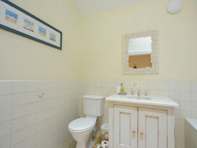 A bathroom with a toilet sink and cabinet a mirror and wall art at Charlton Cottage in Bamburgh