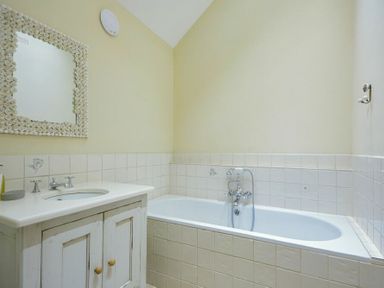 A bathroom with a bathtub and a sink with a mirror above at Charlton Cottage in Bamburgh