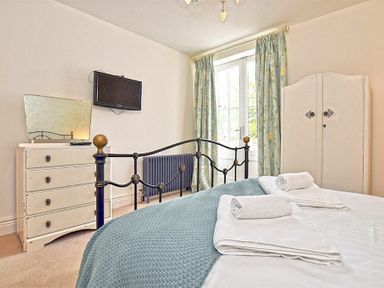 A bedroom with a bed with white towels on it a dresser with a mirror a wall-mounted TV curtains and a wardrobe at Charlton Cottage in Bamburgh
