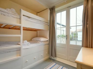 A bedroom with white bunk beds next to glass doors with curtains at Charlton Cottage in Bamburgh