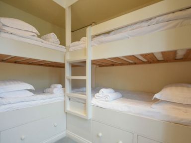 A bedroom with two sets of white bunk beds with folded towels on beds at Charlton Cottage in Bamburgh