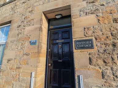 A black door with number 2 and a sign that says Riverside Cottage on a stone wall at Riverside Cottage in Warkworth