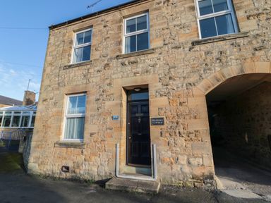The exterior of a stone cottage with a dark door and four windows at Riverside Cottage in Warkworth