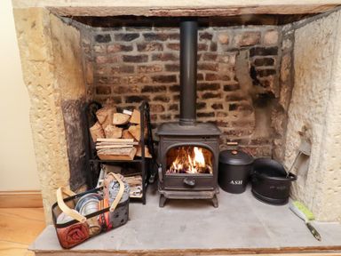 A wood stove with firewood and an ash can at Riverside Cottage in Warkworth