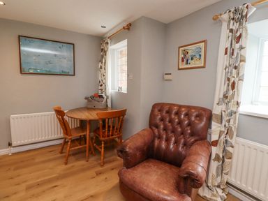 A room with a round wooden table with two wooden chairs and a brown leather armchair at Jara in Bamburgh