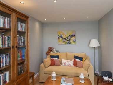 A sitting room with a beige sofa with cushions and stuffed animals a wooden cabinet with DVDs and a floor lamp at Jara Bamburgh