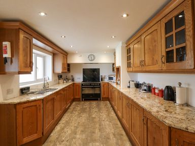 A kitchen with wooden cabinets and granite countertops with a stove at the end at Jara in Bamburgh