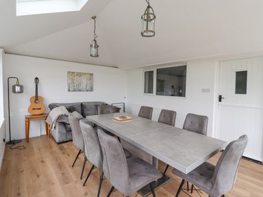 A dining room with a large table and chairs next to a sofa with a guitar on a side table at Jara in Bamburgh
