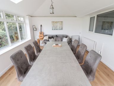 A dining room with a long table surrounded by chairs and a sofa with guitar on a side table at Jara in Bamburgh