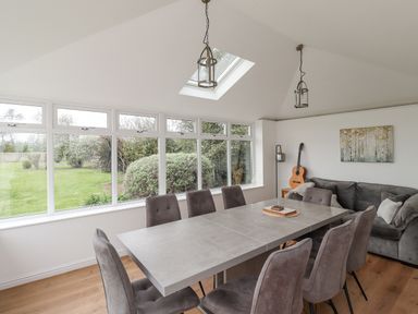 A dining room with gray chairs around a rectangular table and large windows showing a garden at Jara in Bamburgh