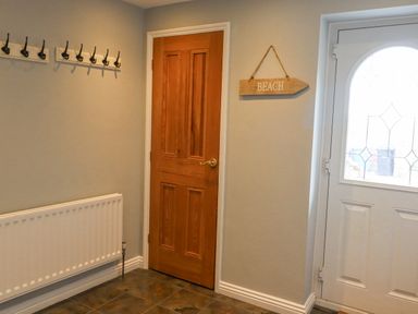 An entryway with a wooden door a white exterior door with patterned glass hooks on the wall and a beach sign at Jara in Bamburgh