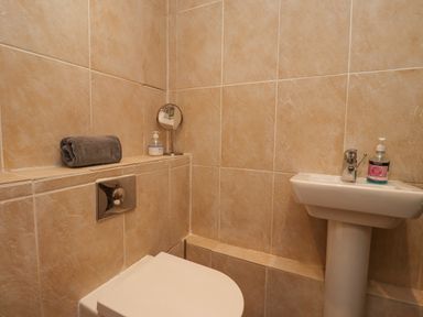 A bathroom with a toilet a pedestal sink a small mirror a rolled towel and soap bottles at Jara in Bamburgh
