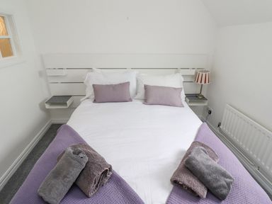 A bedroom with a double bed with white bedding and purple blankets with purple pillows and towels at Jara in Bamburgh