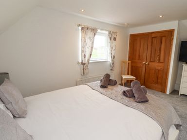A bedroom with a bed and rolled towels near a window and wooden double doors at Jara Bamburgh