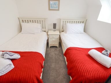 A bedroom with two single beds red blankets white pillows a small white nightstand with a lamp and a framed picture on the wall at Jara in Bamburgh