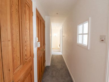 A hallway with wooden doors on the left and a window on the right at Jara in Bamburgh