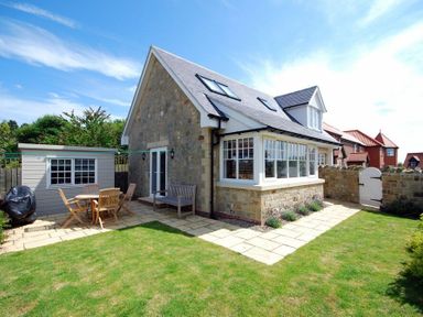 A stone house with patio furniture and shed in a garden at Stone Cottage Bamburgh