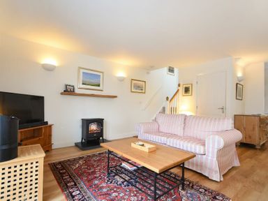 A living room with a striped sofa a wooden coffee table a patterned rug a television and a small fireplace at Stone Cottage in Bamburgh