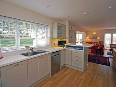 A kitchen with a sink dishwasher and countertop opening into a living room at Stone Cottage in Bamburgh