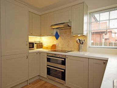 A kitchen corner with beige cabinets a double oven a stovetop a microwave a bread bin cooking utensils and a window at Stone Cottage Bamburgh