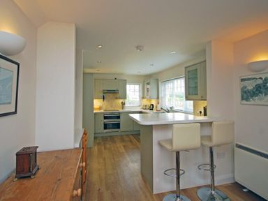 A kitchen with green cabinets two white bar stools a wooden table and framed pictures at Stone Cottage in Bamburgh
