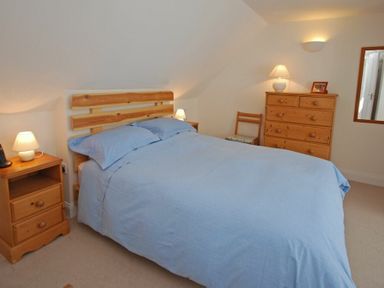 A bedroom with a wooden bed frame blue bedding wooden dressers lamps and a mirror at Stone Cottage in Bamburgh