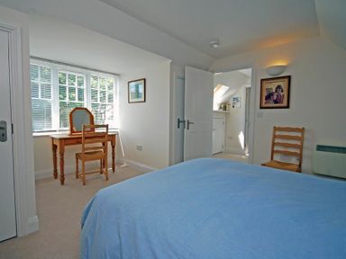 A bedroom with a blue bedspread a wooden chair and dressing table near a window at Stone Cottage in Bamburgh