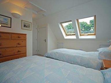 A bedroom with two single beds a wooden chest of drawers and two skylight windows at Stone Cottage in Bamburgh