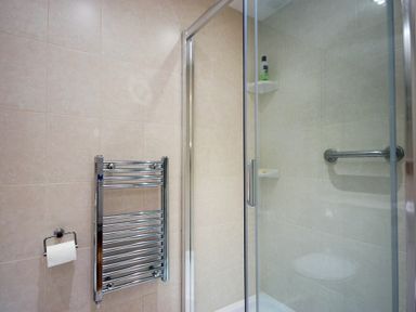 A bathroom with a glass shower enclosure a metal towel radiator and a toilet paper holder at Stone Cottage in Bamburgh