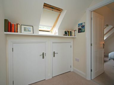 A hallway with two small closed doors and shelves with books beneath a skylight window at Stone Cottage in Bamburgh