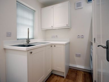 A utility room with a sink cabinet a wall cabinet a window with blinds and a washing machine at Stone Cottage in Bamburgh