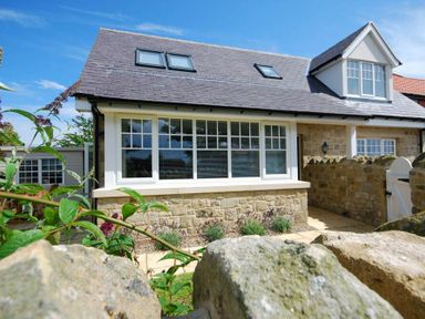 A stone house with large windows and a gated stone wall at Stone Cottage in Bamburgh