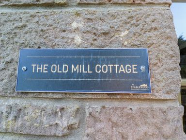 A sign for The Old Mill Cottage at Stablewood Coastal Cottages in Lucker