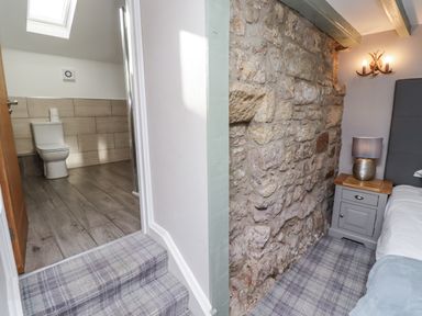 A bathroom with a toilet and shower next to a bedroom with a stone wall at Old Mill in Lucker