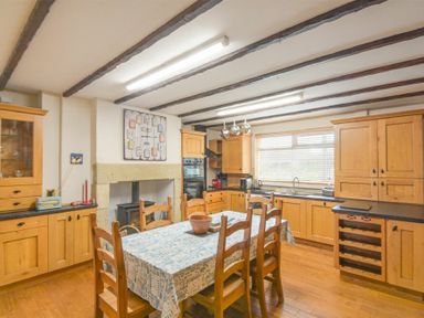 A kitchen with wooden cabinets a dining table with chairs and a window at Creel Cottage Amble
