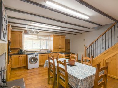A kitchen with wooden cabinets a dining table with six chairs and kitchen appliances at Creel Cottage Amble