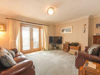 A living room with leather sofas TV and wooden doors with curtains at Creel Cottage Amble